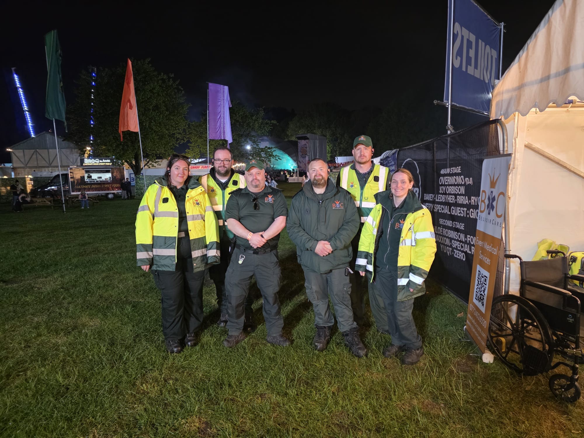The BelvoirCare medical team on duty in branded hi-vis jackets beside their medical tent at a night-time festival.