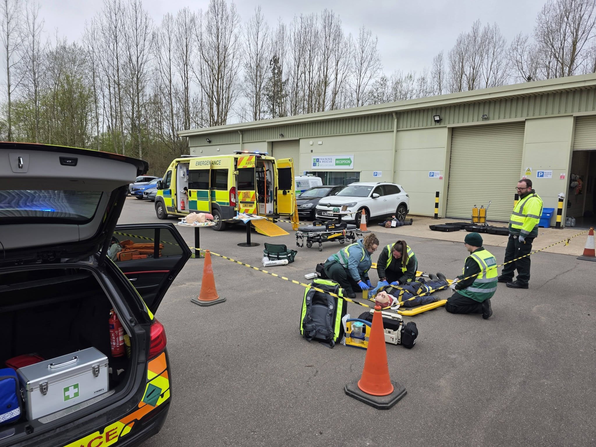 BelvoirCare medics running a scenario-based training exercise, treating a patient on a stretcher beside an ambulance.