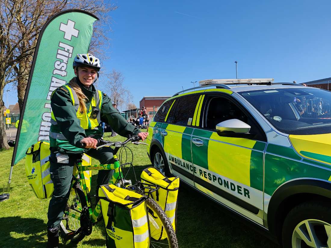 A BelvoirCare medic with the Cycle Response Unit bike beside an ambulance-responder vehicle.